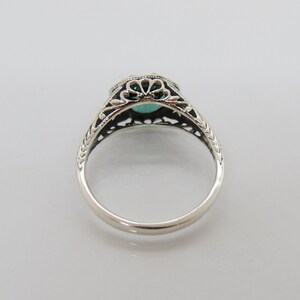 May include: A silver ring with an ornate filigree design and a green gemstone in the center.