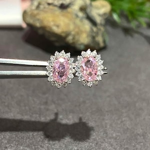 May include: A pair of silver earrings with pink oval-shaped gemstones surrounded by smaller clear gemstones.
