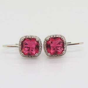 May include: A pair of silver earrings with a square-shaped pink gemstone surrounded by a halo of smaller clear gemstones.