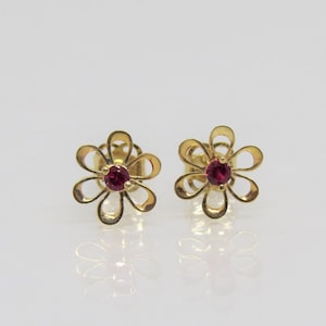 May include: A pair of gold flower-shaped earrings with red gemstones in the centre.
