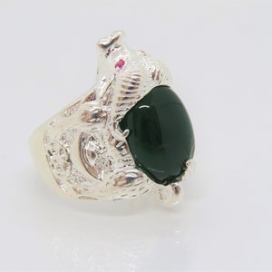May include: A silver ring with a green gemstone and a detailed design of a bear. The bear has a small red gemstone for an eye.