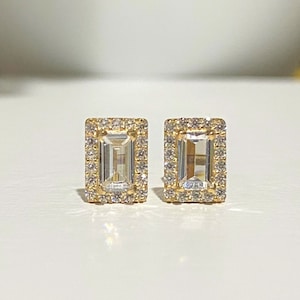 May include: A pair of gold earrings with a rectangular emerald-cut clear stone set in a halo of smaller clear stones.