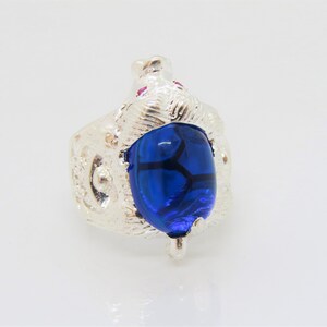 May include: A silver ring with a blue beetle design. The beetle has a detailed, textured body and a large, blue gemstone.
