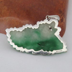 Pode incluir: Um pingente de jade verde com uma configura&ccedil;&atilde;o de prata. O pingente tem a forma de uma folha e apresenta um design detalhado. A parte de tr&aacute;s do pingente &eacute; vis&iacute;vel, mostrando a configura&ccedil;&atilde;o de prata e a pedra de jade.