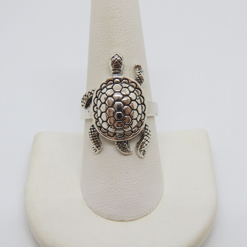 May include: A silver ring featuring a detailed turtle design. The turtle's shell is textured with a honeycomb pattern.
