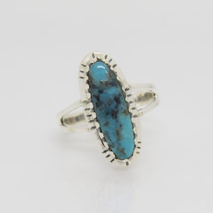 May include: A silver ring with a turquoise oval stone set in a silver bezel. The stone has a blue and green color with black veins.