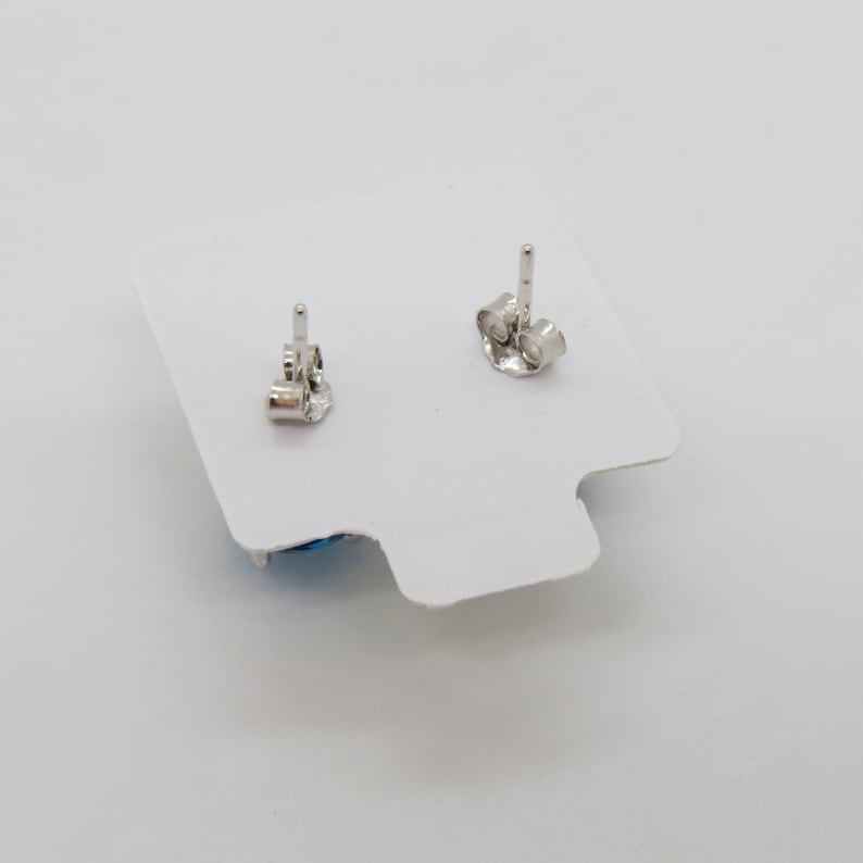 Puede incluir: Un par de pendientes de plata con piedras azules. Los pendientes est&aacute;n sobre un fondo blanco.