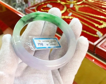 May include: A jadeite jade bangle bracelet with a green and white color gradient. The bracelet is labeled "NATURAL JADETTE JADE N°: 249023" with a "PNJ" logo.