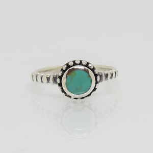 Peut inclure: Une bague en argent avec une pierre turquoise sertie dans une bélière perlée. La bande est texturée avec de petites perles.