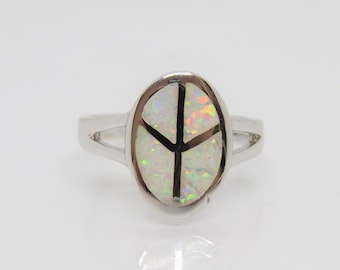 Puede incluir: Un anillo de plata con una piedra ovalada de ópalo blanco engastada en el centro. La piedra tiene un diseño de signo de paz en negro.