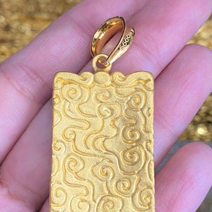 Pu&ograve; includere: Ciondolo in oro di forma rettangolare con un motivo a spirale dettagliato. Il ciondolo ha un anello nella parte superiore per attaccarlo a una catena. Il ciondolo &egrave; contrassegnato dal numero "9999".