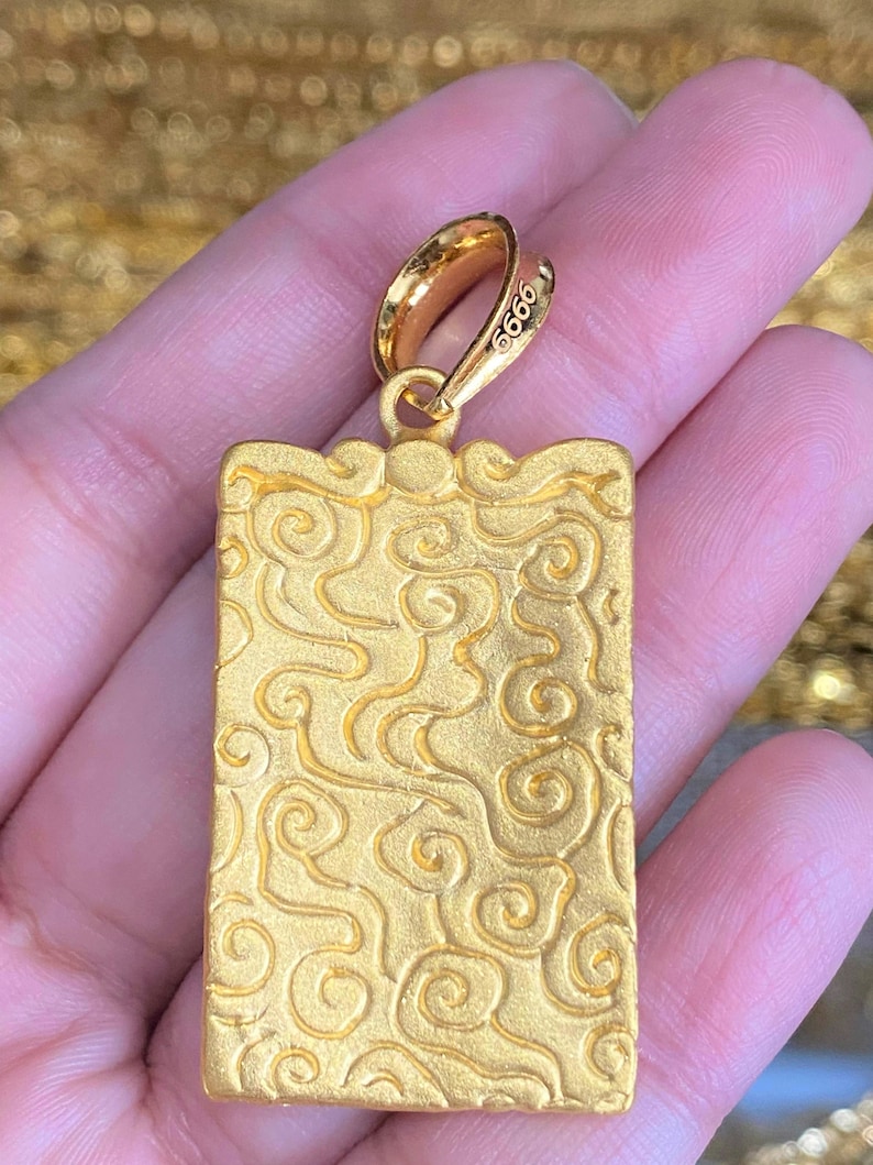Pu&ograve; includere: Ciondolo in oro di forma rettangolare con un motivo a spirale dettagliato. Il ciondolo ha un anello nella parte superiore per attaccarlo a una catena. Il ciondolo &egrave; contrassegnato dal numero "9999".