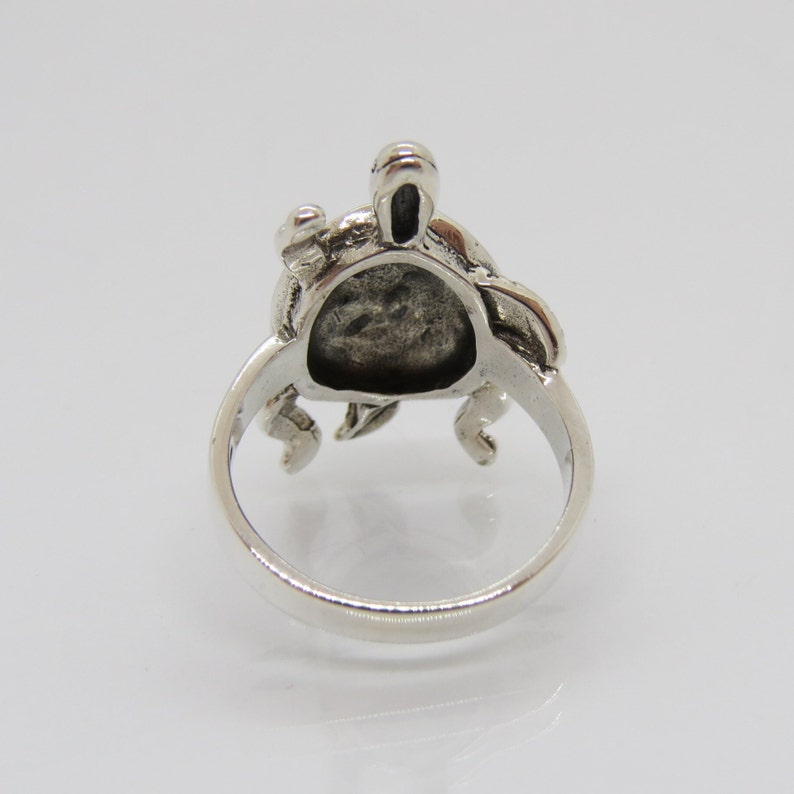 May include: Silver ring featuring a detailed turtle design. The turtle is facing forward with its head raised and its legs outstretched. The ring is made of sterling silver and has a polished finish.