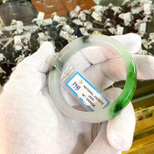 Può includere: Un braccialetto bianco in giadeite con vortici verdi e bianchi. Il braccialetto è etichettato "NATURAL JADEITE JADE" e "N°: 249004".