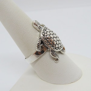 May include: Silver ring featuring a detailed turtle design. The turtle is facing to the right and has a textured shell.