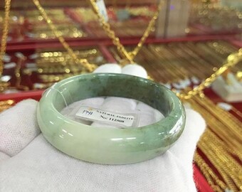 Puede incluir: Un brazalete de jadeíta verde sobre un fondo blanco. El brazalete tiene una etiqueta de jadeíta natural con el texto "NATURAL JADEITE No. 112508".