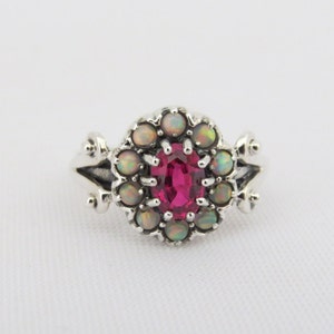 May include: A silver ring with a pink oval gemstone surrounded by a halo of white opals.