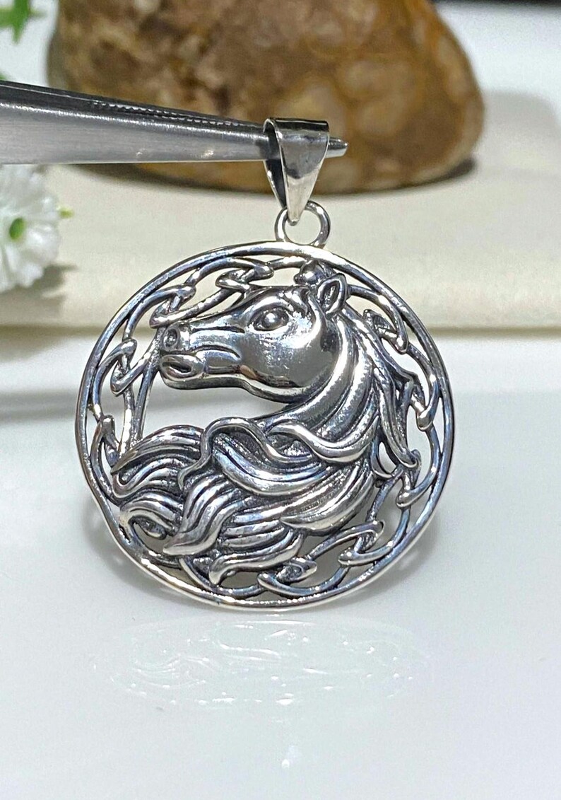 May include: Silver pendant featuring a detailed Celtic knot design with a horse's head in the center.