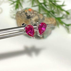 May include: A pair of silver stud earrings with pear-shaped red gemstones.