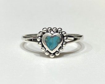 May include: A silver ring with a turquoise heart-shaped stone surrounded by a beaded halo.