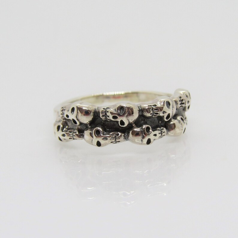 May include: A silver ring with a band of skulls. The skulls are arranged in a row around the band, and they are all facing the same direction.