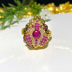 Peut inclure: Une bague en or avec une grande pierre précieuse rose entourée de petites pierres précieuses roses et blanches. La bague a un design délicat et complexe.