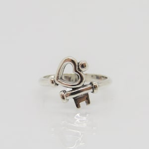 Puede incluir: Un anillo de plata con un diseño de llave en forma de corazón.