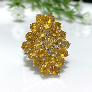 May include: A silver ring with a cluster of yellow citrine gemstones. The ring is set with a large number of small, round stones, creating a dense and sparkling effect.