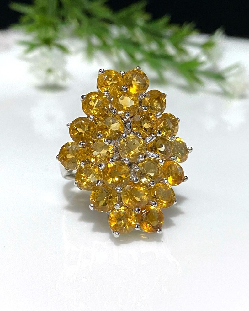 May include: A silver ring with a cluster of yellow citrine gemstones. The ring is set with a large number of small, round stones, creating a dense and sparkling effect.