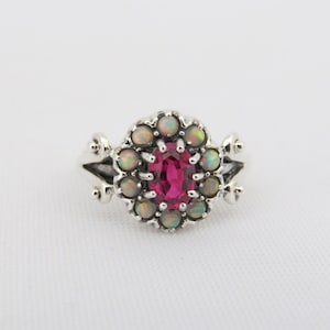 May include: A silver ring featuring a pink oval gemstone encircled by a halo of white opals.