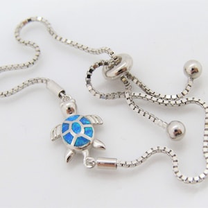May include: A silver adjustable bracelet with a blue opal turtle charm. The bracelet has a sliding clasp and is made of a delicate chain.