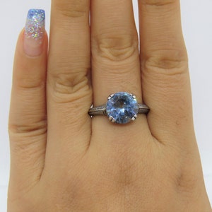 May include: A silver ring featuring a large, round, light blue gemstone. The ring has a detailed, engraved band.
