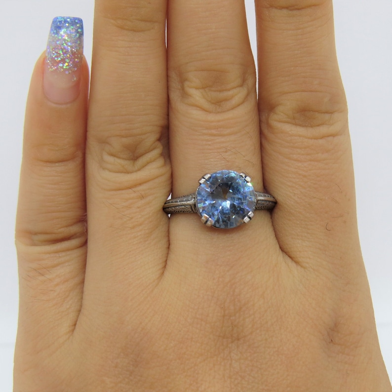 May include: A silver ring featuring a large, round, light blue gemstone. The ring has a detailed, engraved band.