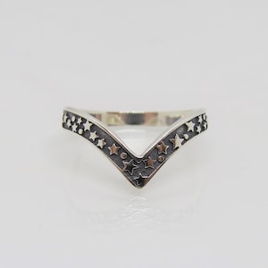 May include: A silver ring with a V-shaped band decorated with small stars. The stars are raised and have a slightly darker finish than the rest of the ring.