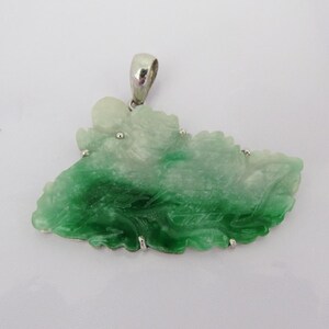Pode incluir: Um pingente de jade verde e branco esculpido em forma de folha, engastado em prata com uma argola de prata.