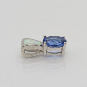 Op de afbeelding: Een zilveren hanger met een ovale, blauwe edelsteen en een kleinere, witte opaalsteen. De blauwe steen is gezet in een vier-klauwzetting. De hanger heeft een lus voor een ketting.