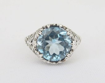 May include: A silver ring with a large, round, light blue topaz gemstone set in a filigree design.