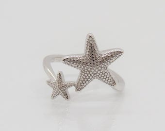 May include: Silver ring with two starfish designs. The larger starfish is on the top and the smaller starfish is on the bottom.
