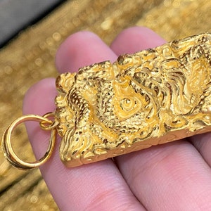 Pu&ograve; includere: Un ciondolo d'oro con un designo di drago dettagliato. Il ciondolo ha un anello per attaccarlo a una catena.