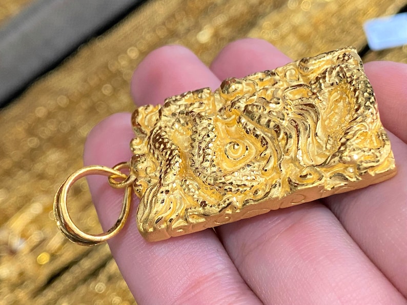 Pu&ograve; includere: Un ciondolo d'oro con un designo di drago dettagliato. Il ciondolo ha un anello per attaccarlo a una catena.