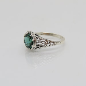 May include: A silver ring with an emerald green gemstone set in a filigree design.