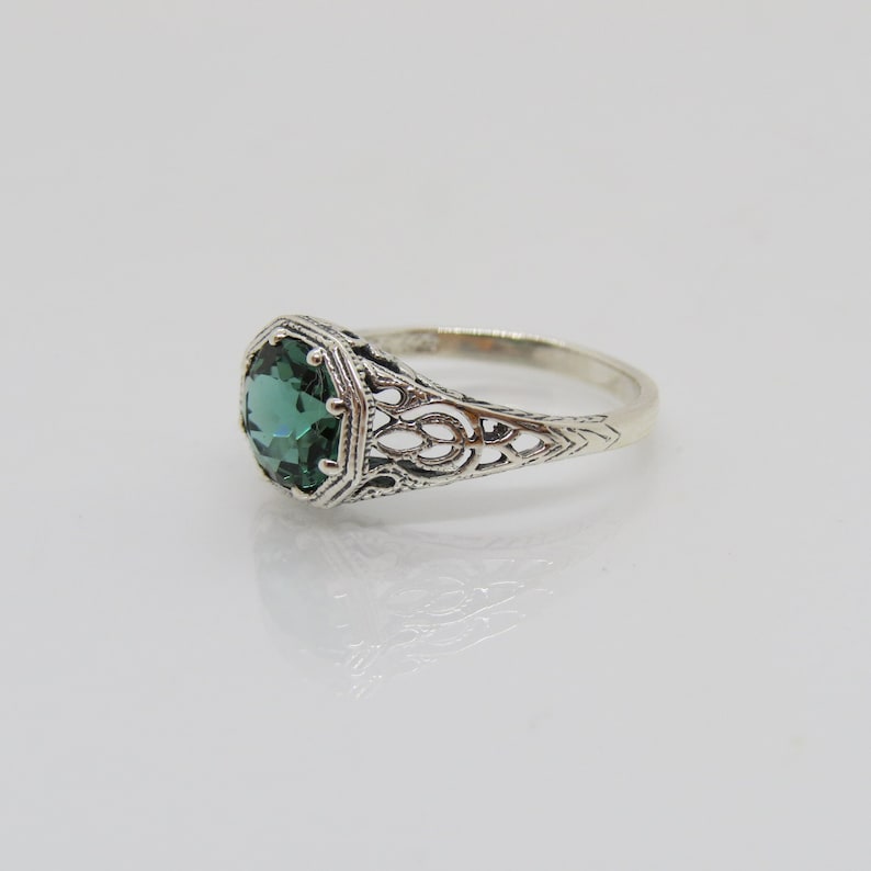 May include: A silver ring with an emerald green gemstone set in a filigree design.