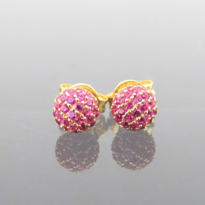 May include: A pair of gold stud earrings with pink gemstones. The earrings are round and have a cluster of small gemstones.