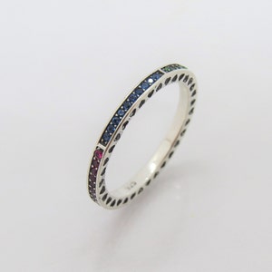 May include: A silver band ring with a row of red, blue, and green gemstones.