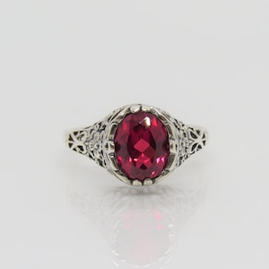 May include: A silver ring featuring an oval red gemstone set in a filigree design.
