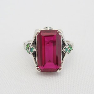 May include: A silver ring with a large, rectangular, pink gemstone surrounded by smaller green gemstones.
