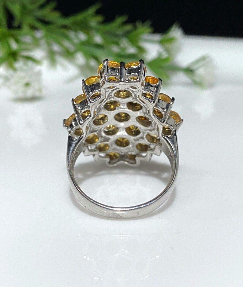 May include: A silver ring with a cluster of yellow gemstones set in a flower-like design. The ring is shown from the back, revealing the band and the setting.