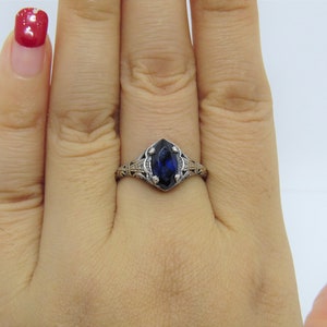 May include: A silver ring with a marquise-shaped blue sapphire gemstone set in a filigree design.