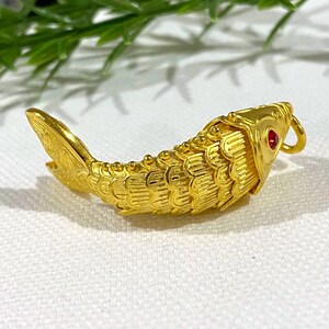 Puede incluir: Un amuleto de pez de color dorado con un ojo de piedra roja. El pez est&aacute; detallado con escamas y tiene un bucle para sujetarlo a una cadena o pulsera.