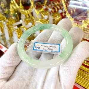 May include: A green jadeite jade bangle bracelet with a white background. The bracelet has a tag attached that reads "NATURAL JADEITE JADE N.: 230084".